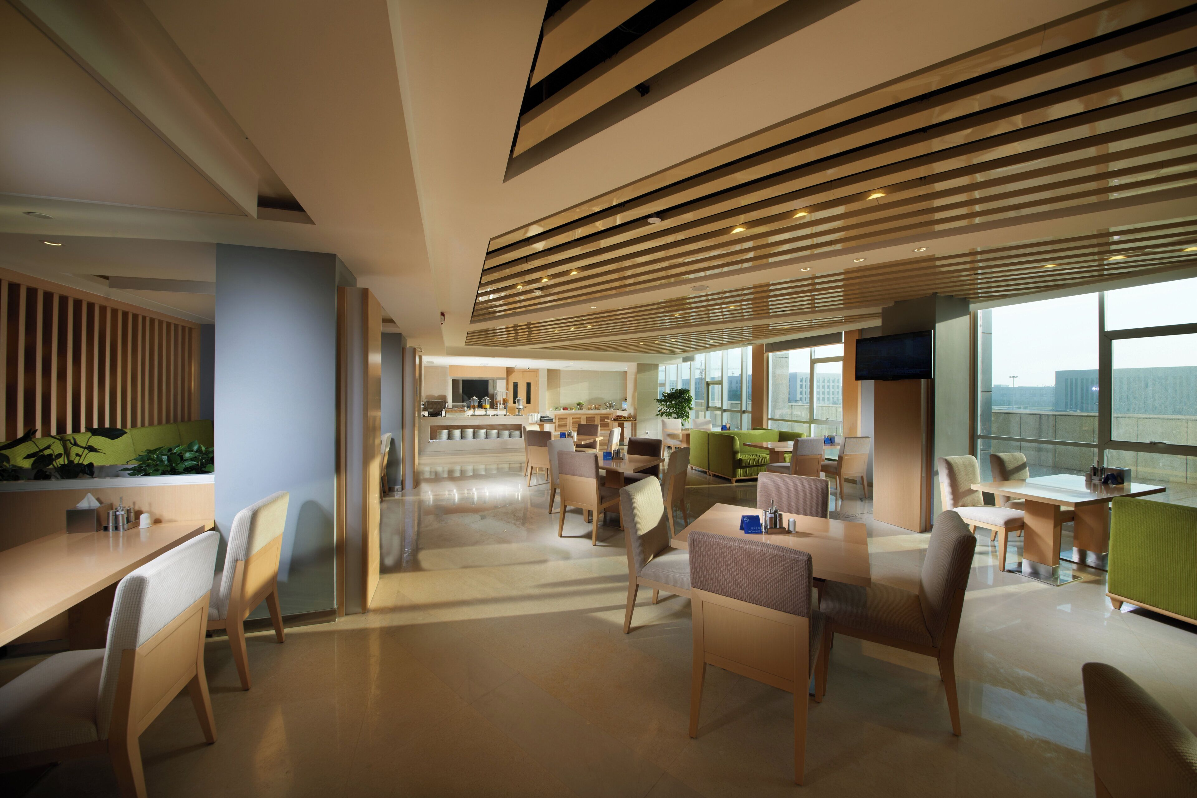 A modern hotel lobby with a central reception desk, seating areas, and large windows offering a city view.