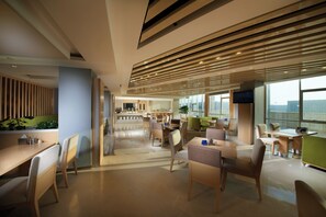 Een moderne hotelentree met een centraal gelegen receptiebalie, zithoeken en grote ramen met uitzicht op de stad.