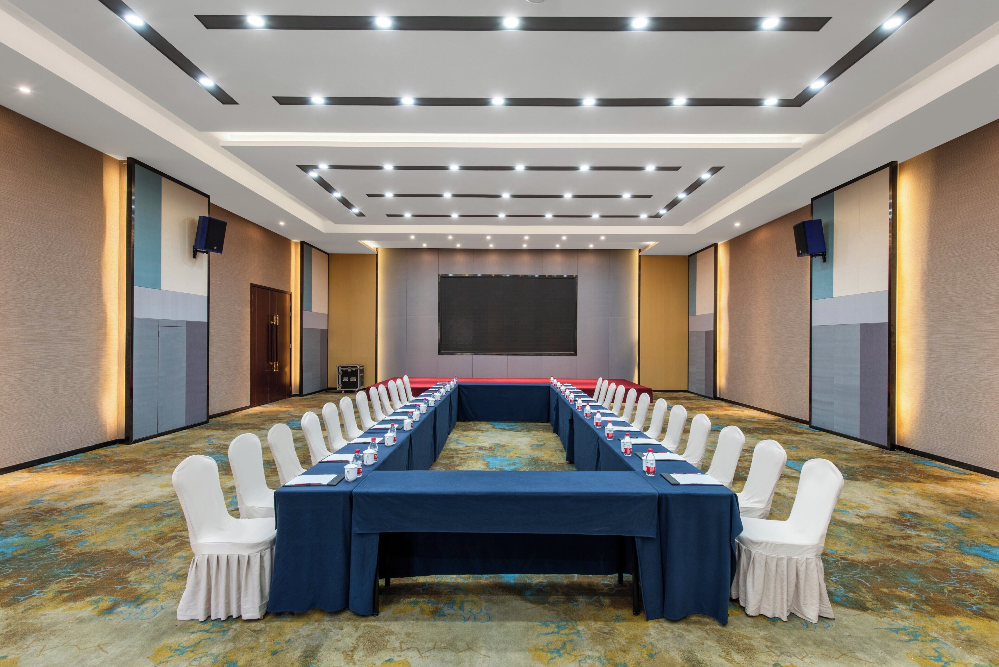 A conference room with a long table, white chairs, and a projector screen.