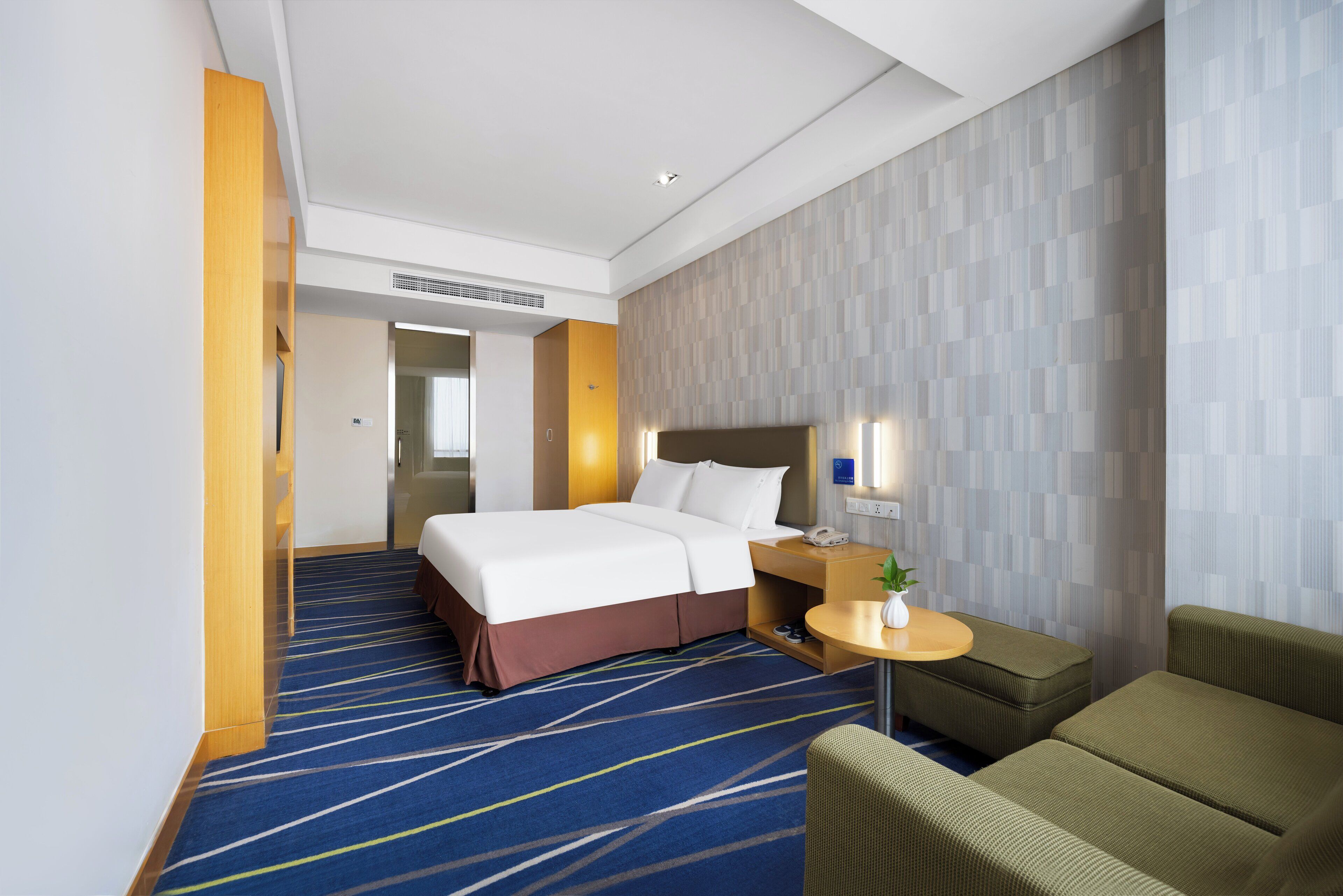 A hotel room with a bed, a desk with a chair, a small table with a plant, and a sofa.