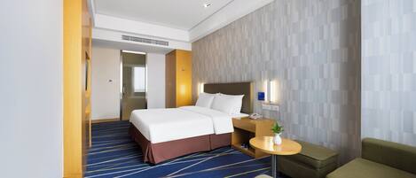 A hotel room with a bed, a desk with a chair, a small table with a plant, and a sofa.