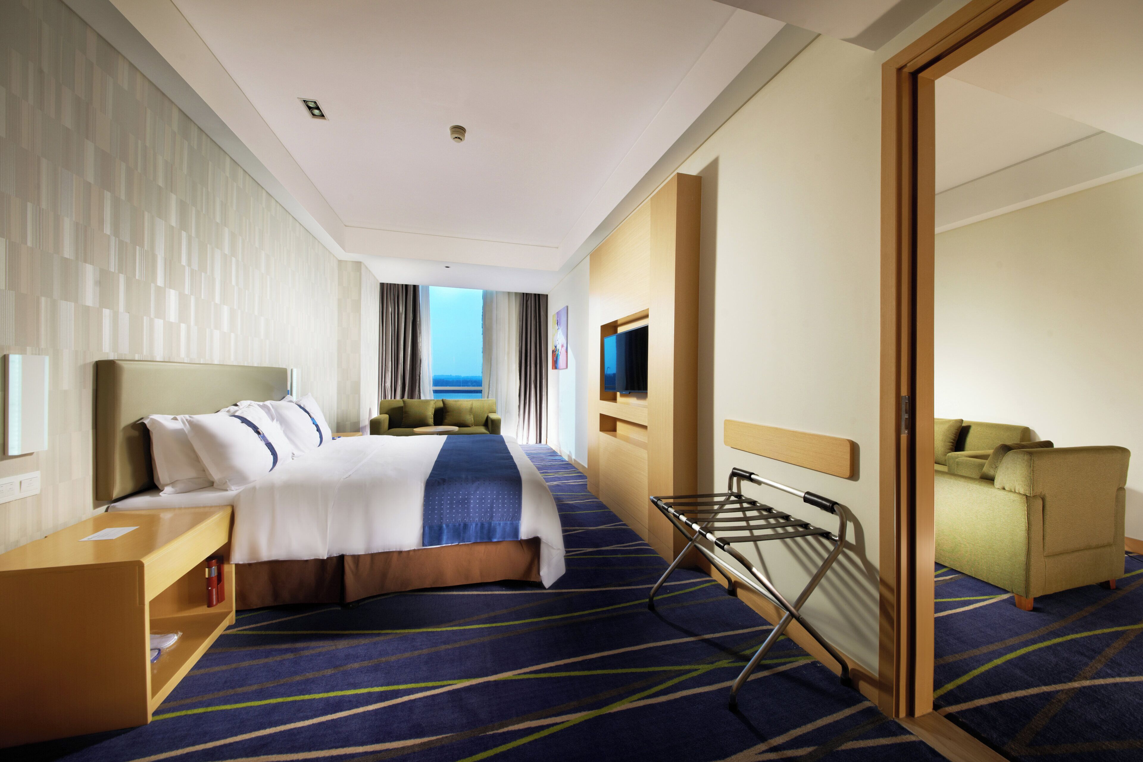 A hotel room with a bed, a seating area, a TV, and a view of the sea.