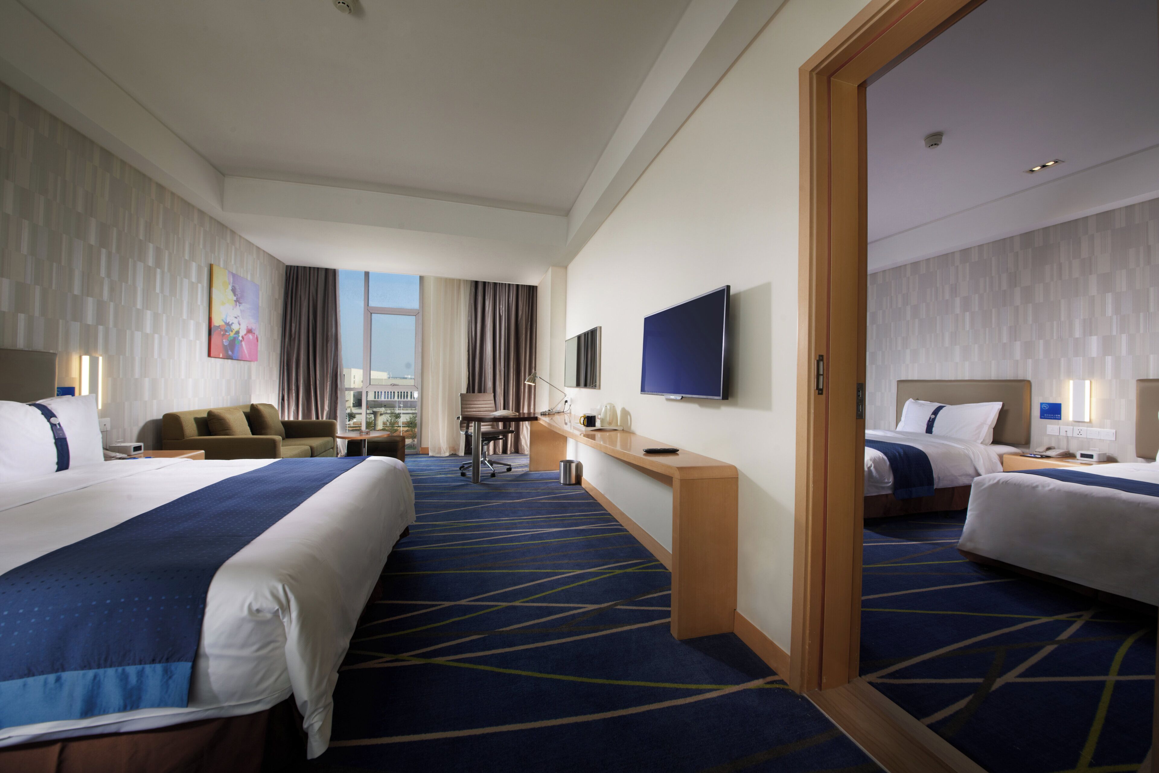 A hotel room with two beds, a desk, a chair, a television, and a view of the city.