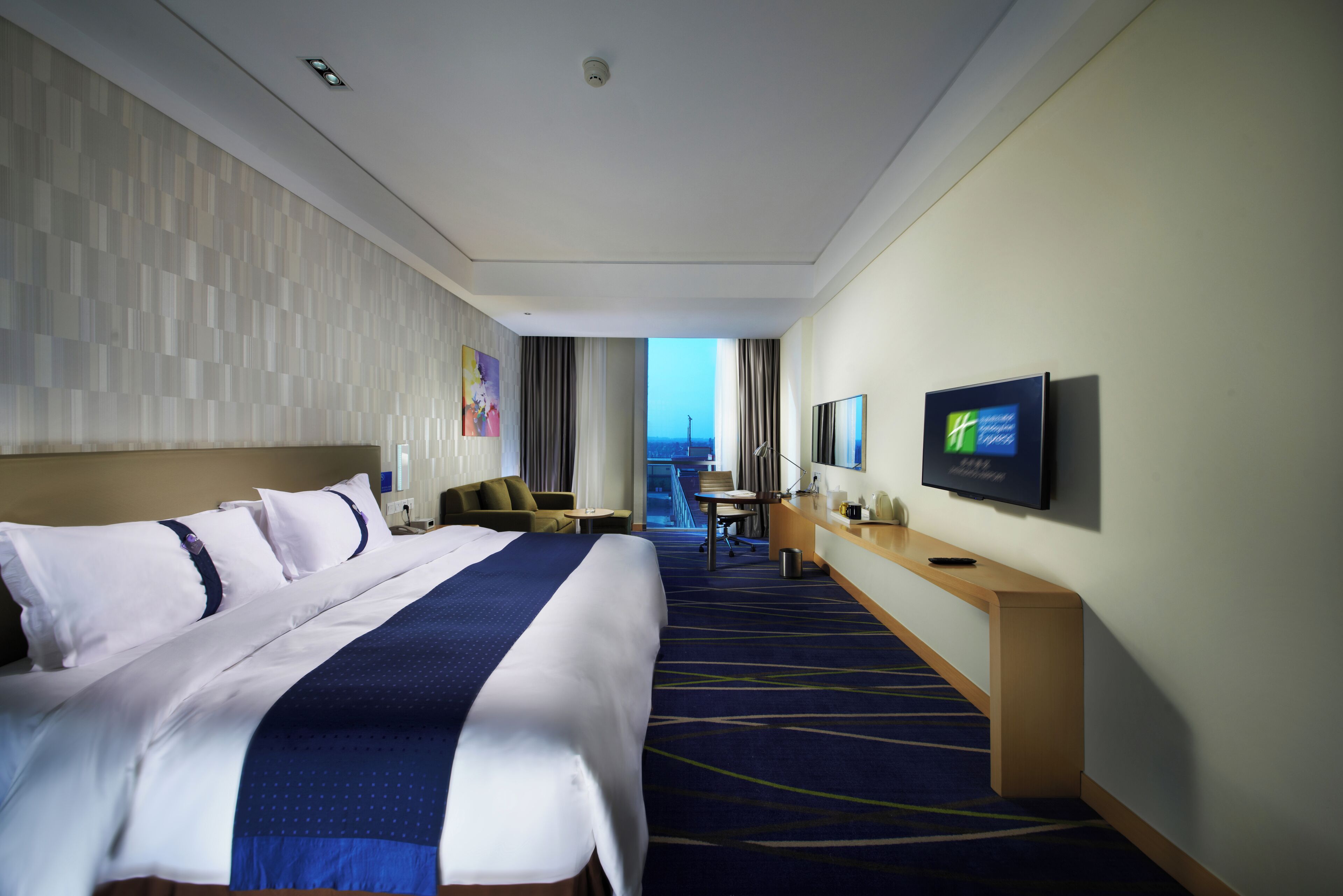 Habitación de hotel con una cama grande, un escritorio, un televisor y vistas a la ciudad.