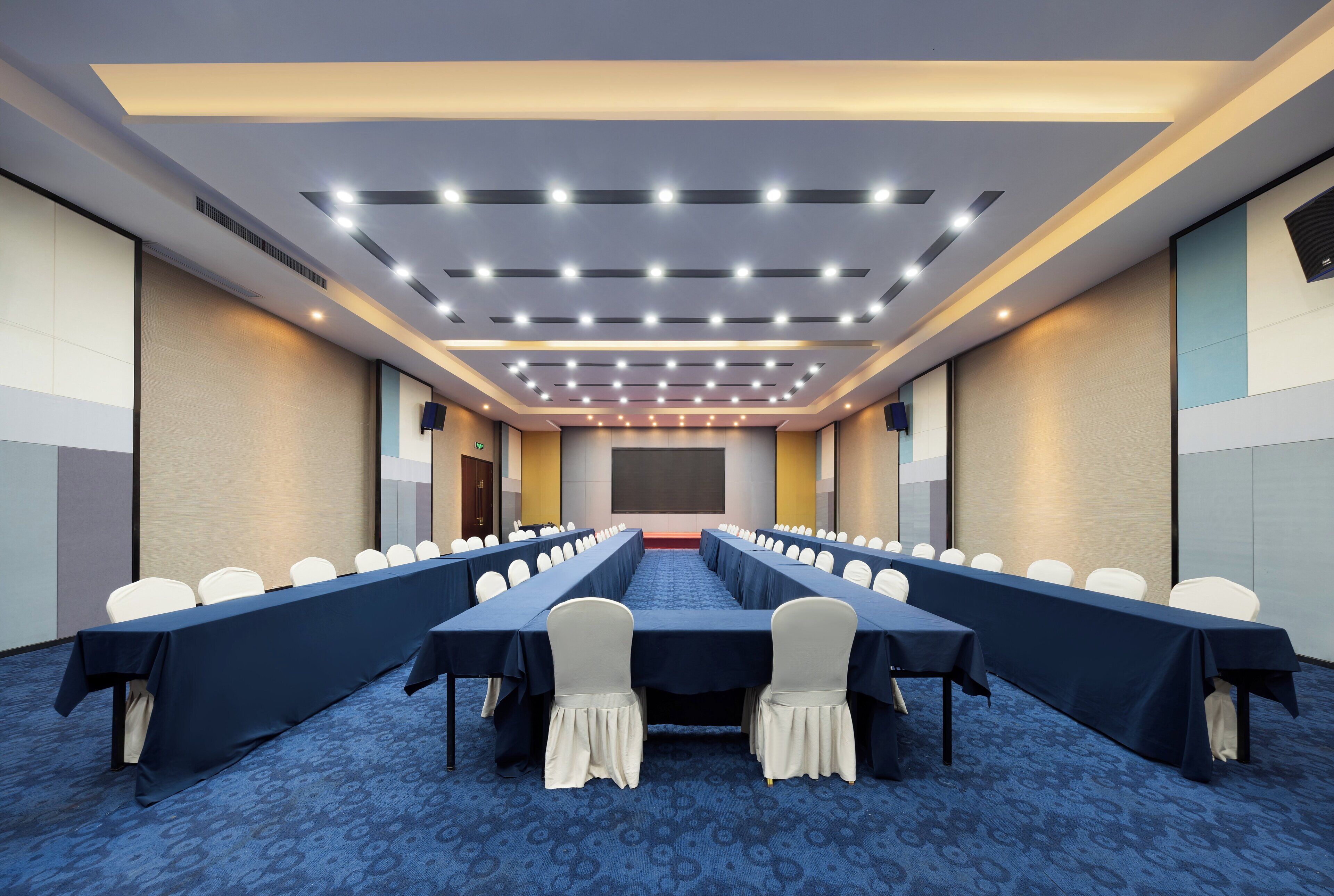 Una sala de conferencias con una larga mesa, filas de sillas y una pantalla para proyector.