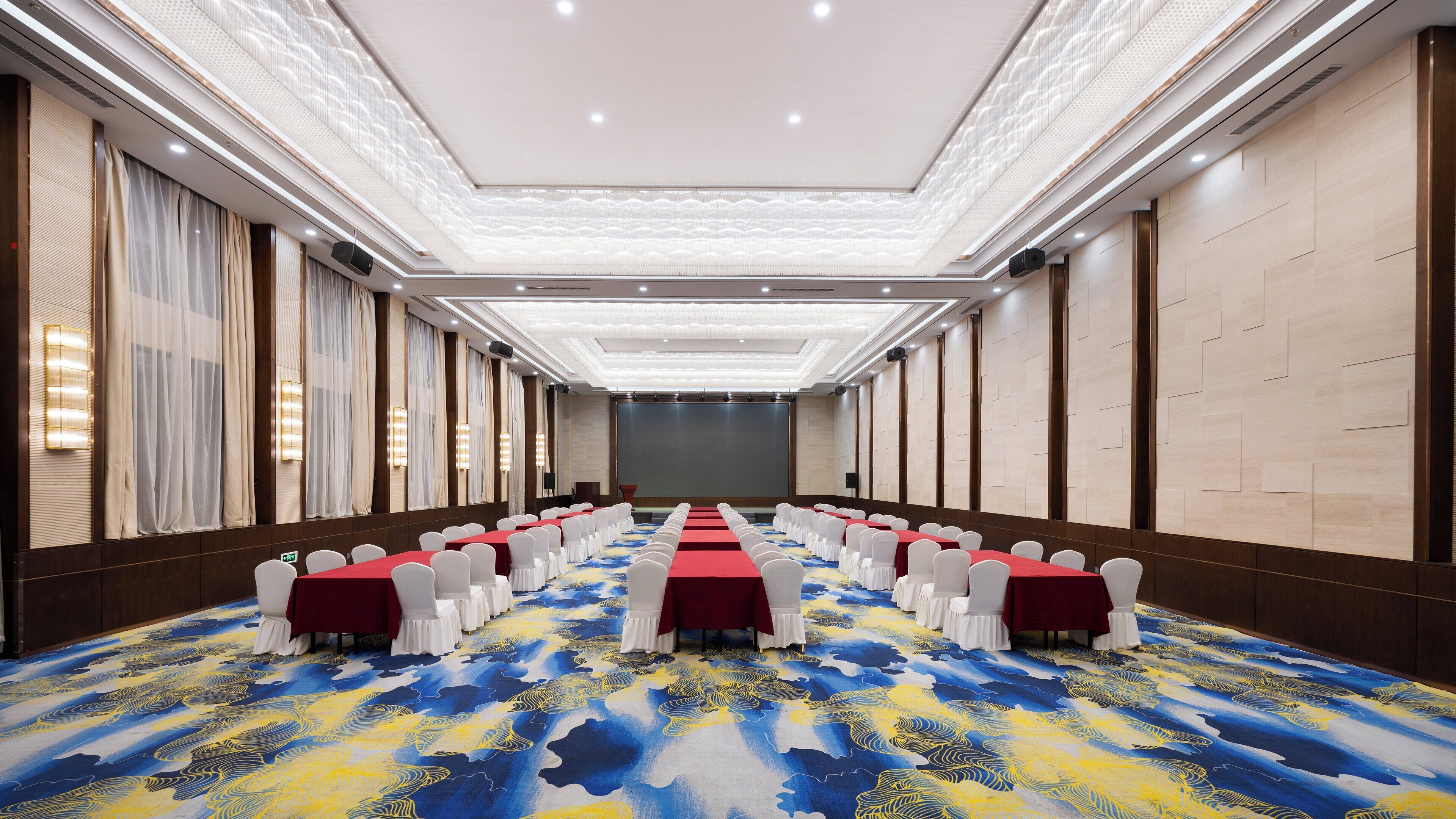 A conference room with rows of tables, white chairs, and a patterned carpet.