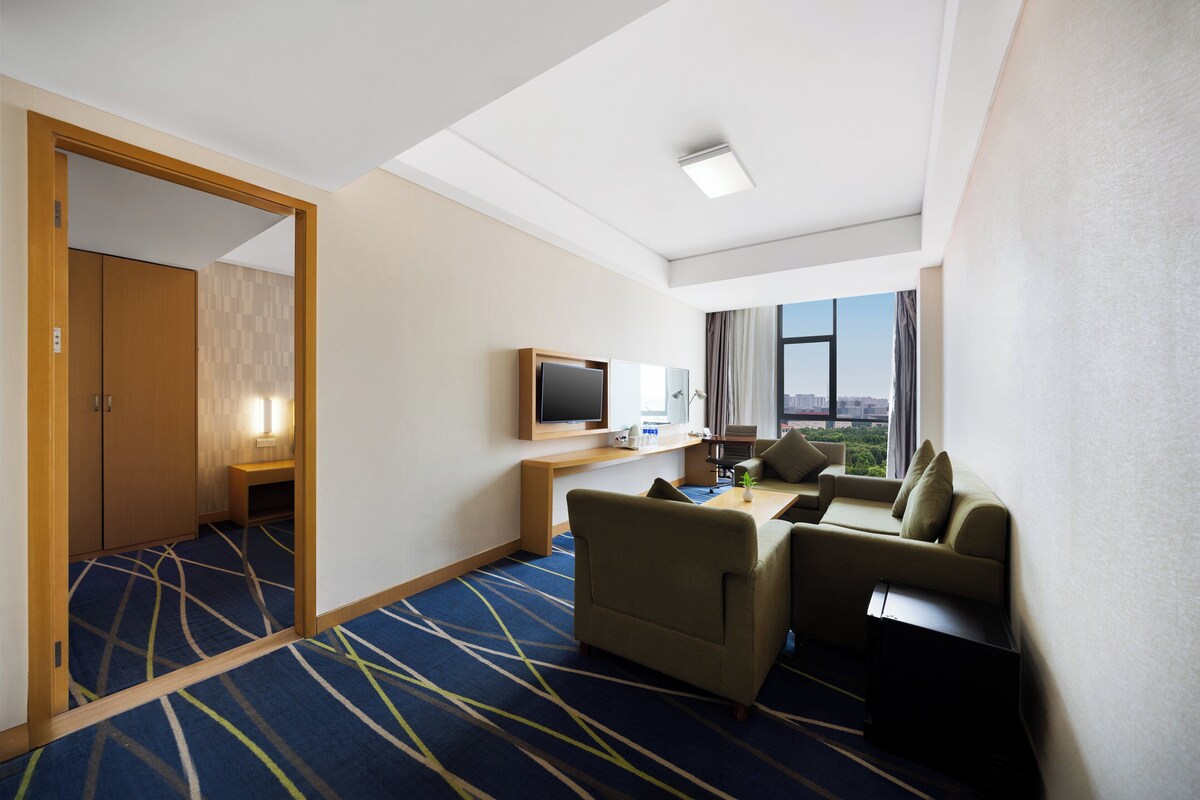 Une chambre d’hôtel avec un canapé, une télévision, un bureau et une vue sur la ville.
