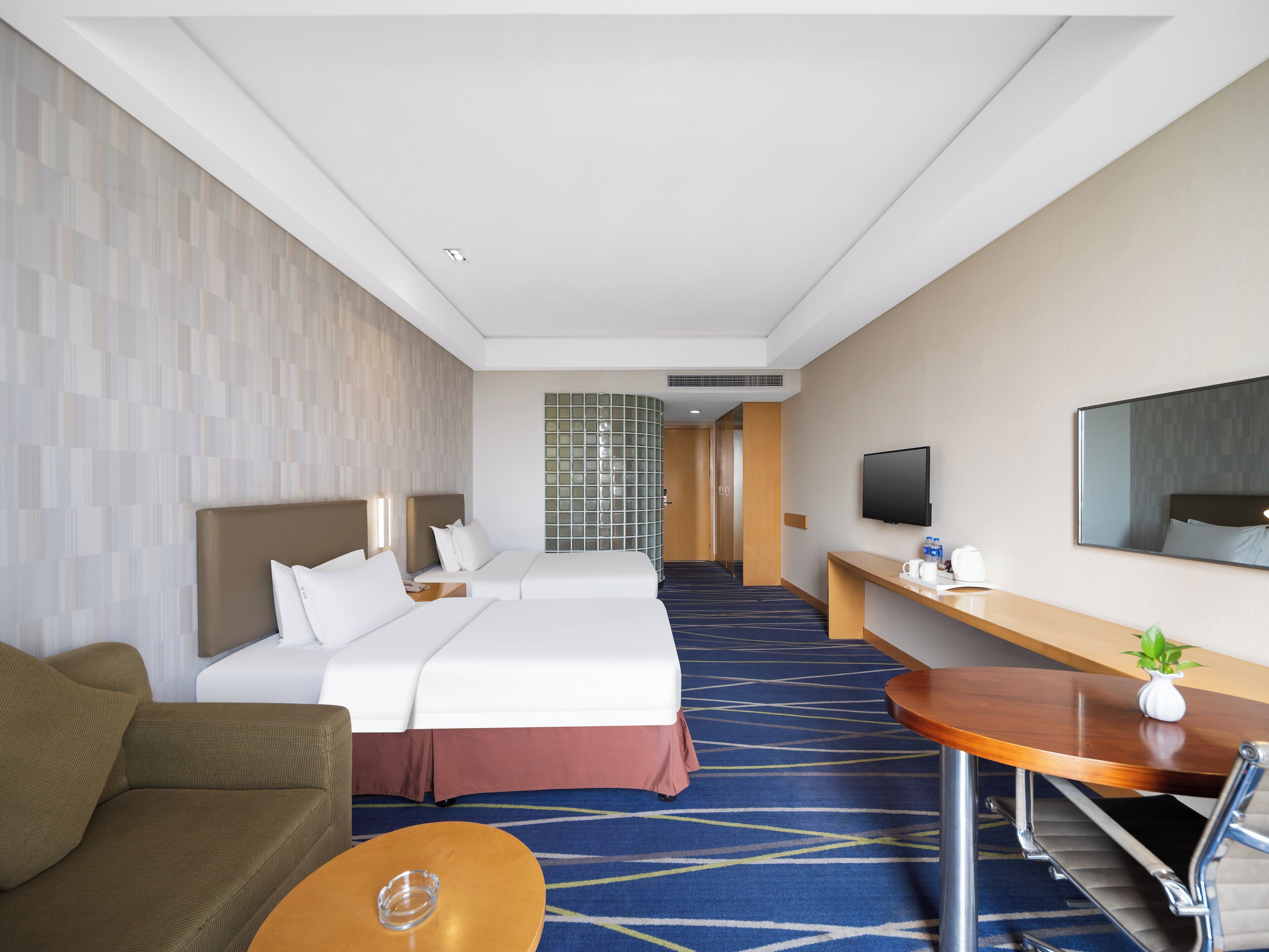 A hotel room with two beds, a sofa, a desk, a TV, and a mirror.