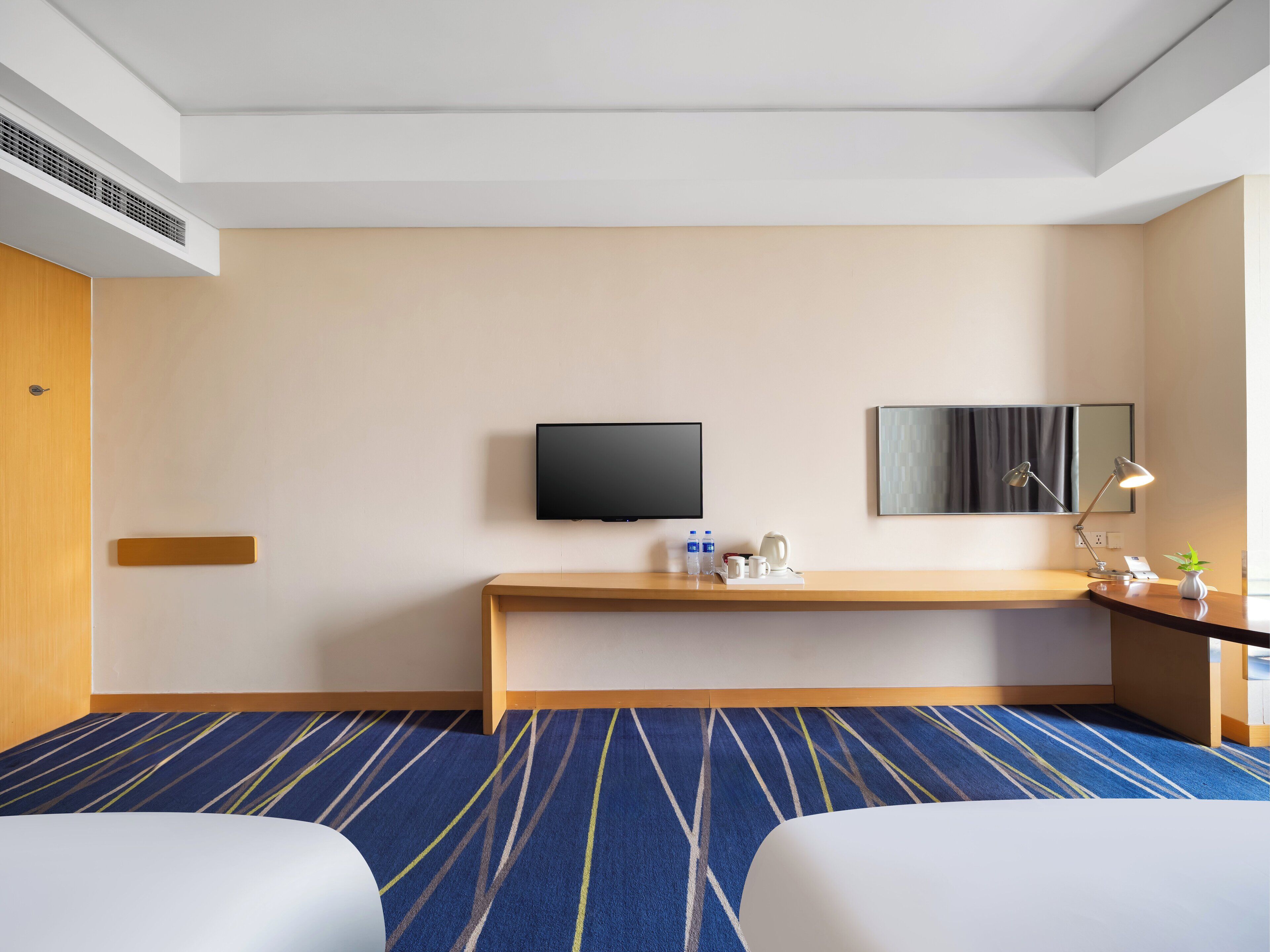 A hotel room with a bed, a desk, a television, a mirror, and a coffee maker.
