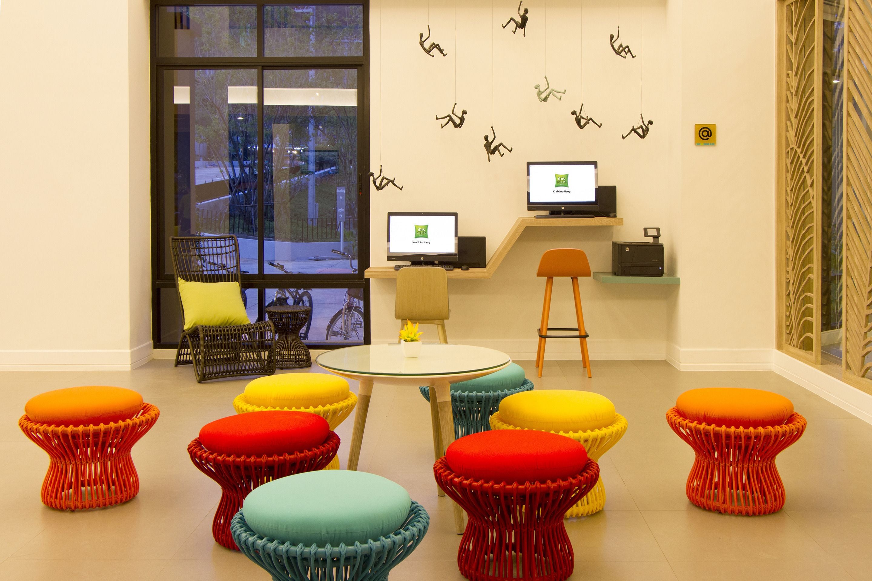 A modern office space with colorful stools, a round table, and two computer monitors on a shelf.