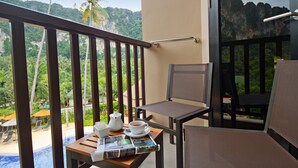 A balcony with a view of a pool and palm trees, a table with a newspaper, a cup of coffee, and a teapot. - ibis Styles Krabi Ao Nang (Krabi)