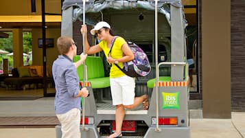 Een tuk-tuk geparkeerd voor een gebouw met een bord waarop 'ibis styles hotels' staat.