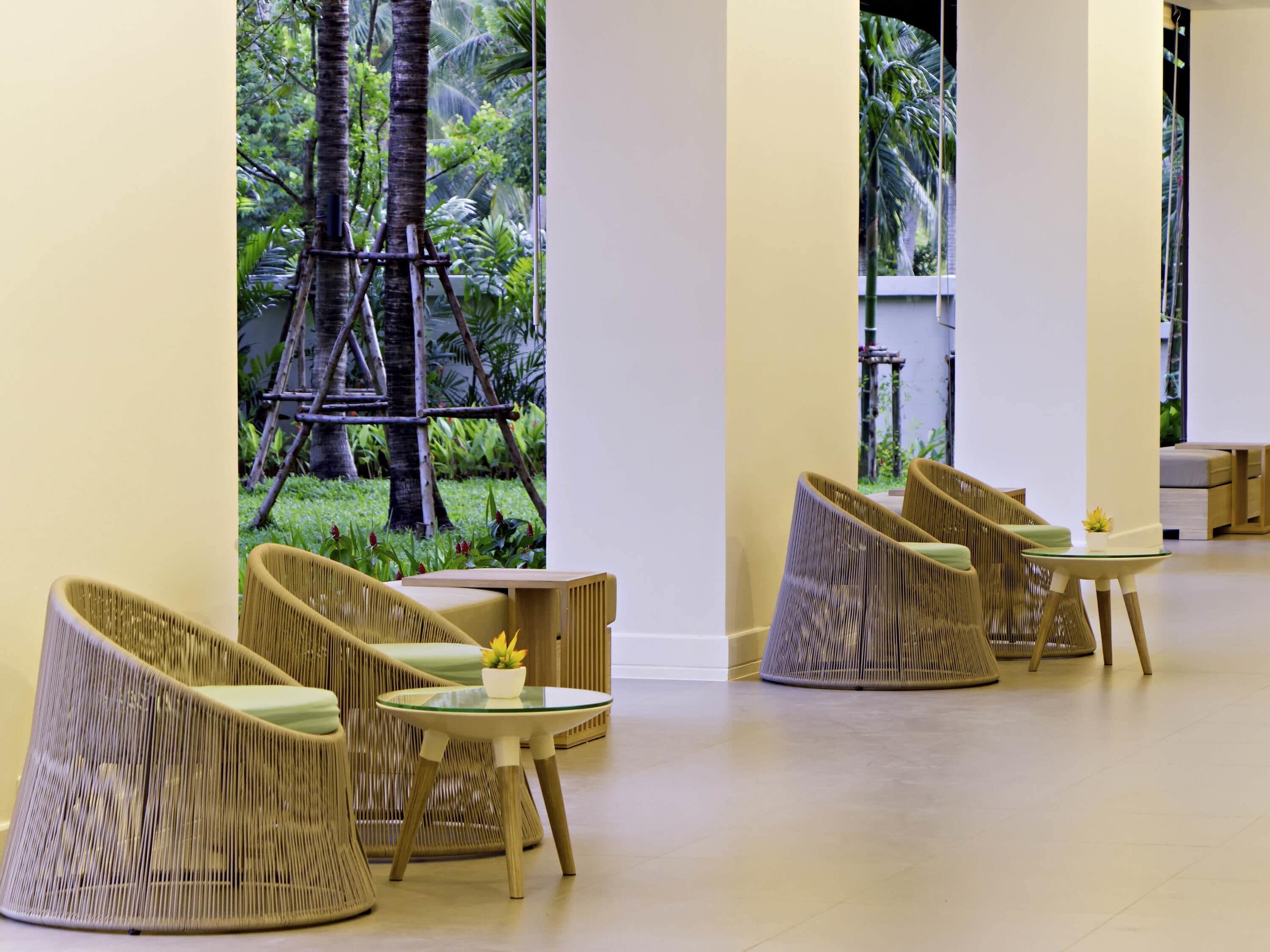 A spacious indoor area with wicker furniture, a small table with a plant, and a view of a tropical garden with a ladder.