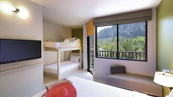 Quarto de hotel com beliches, televisão, janela com vista para o verde e mesa de cabeceira.