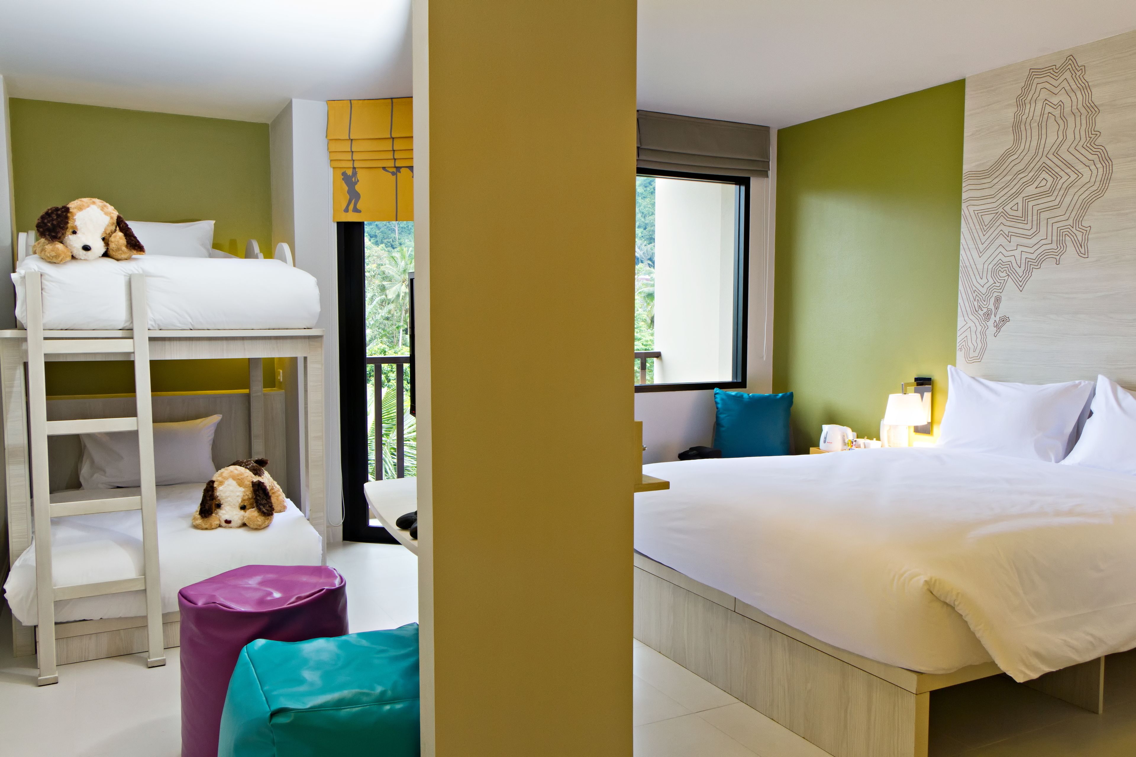 A hotel room with bunk beds, a bed, a window with a view, and a wall with a map design.