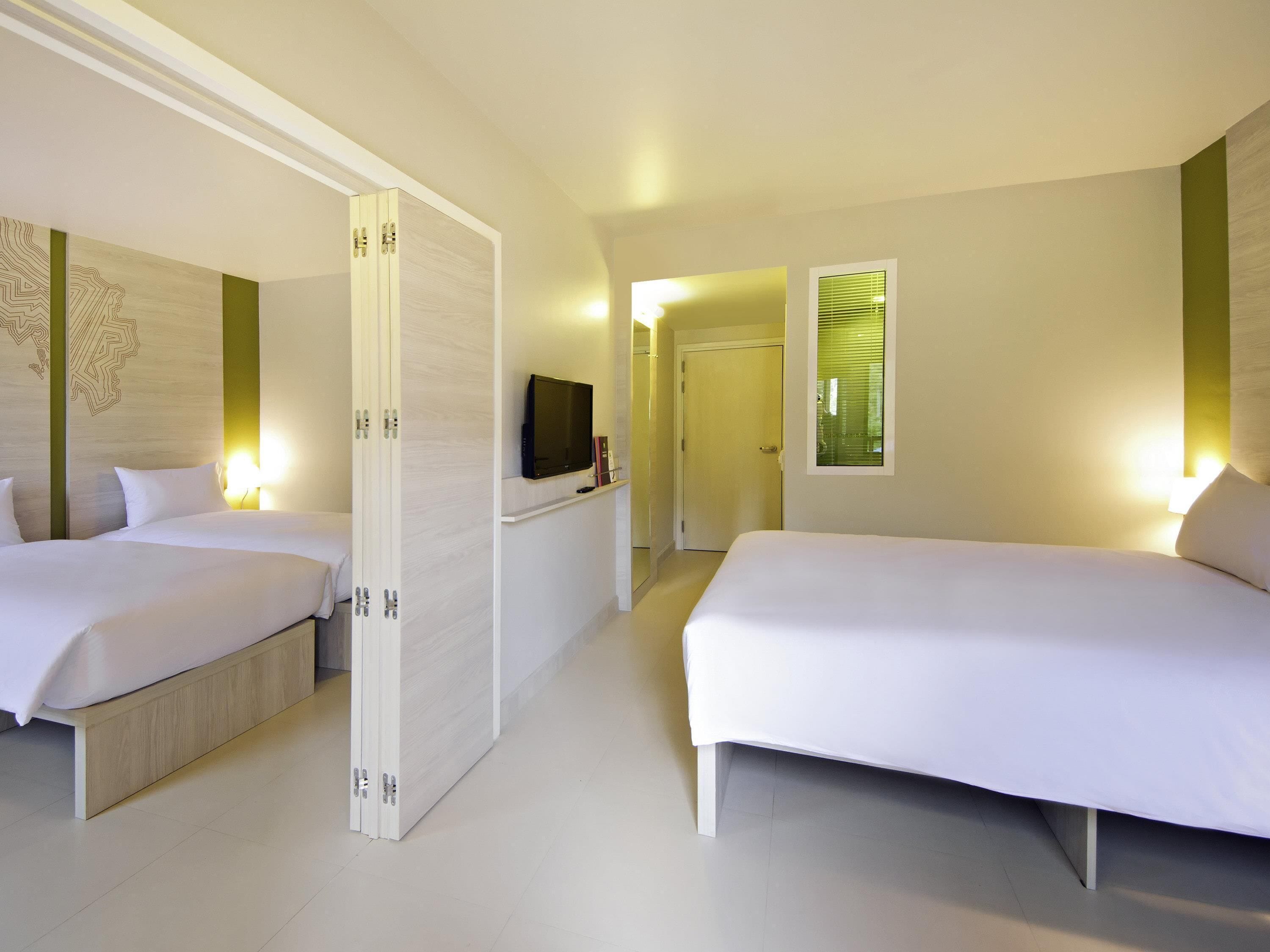 A hotel room with two beds, a television, a door, and a window with blinds.