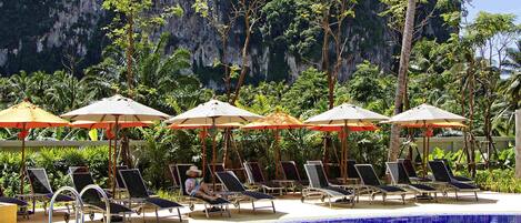 Una piscina al aire libre, sombrillas, sillones reclinables de piscina