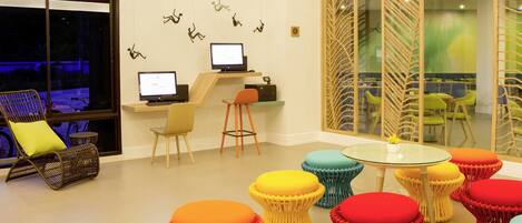 Un área de estar moderna con una mesa de vidrio, taburetes coloridos, computadoras y vistas al exterior.