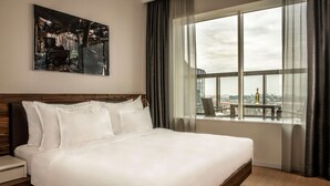 A large bed with white linens, a wooden headboard, and a nightstand with a drawer. A large window with curtains and a view of the city is visible. - Radisson Collection Hotel, Old Mill Belgrade (Belgrade)