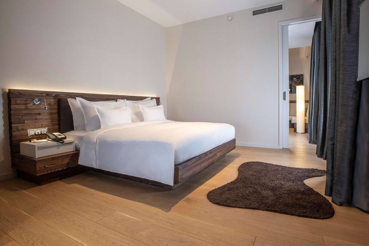 A modern bedroom with a wooden headboard, a bedside table with a lamp, a large bed, and a brown rug.