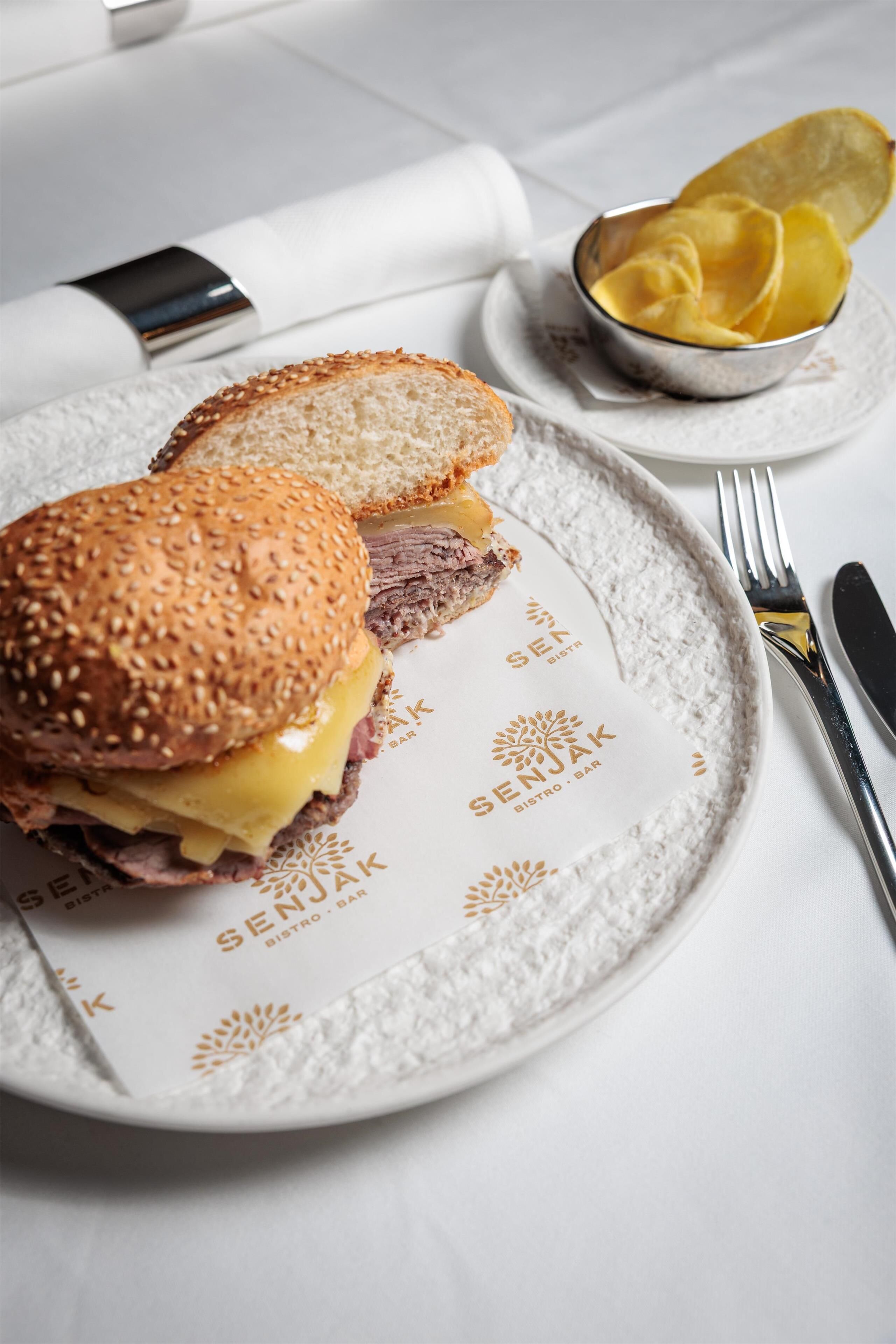 Un plato con un sándwich, un cuenco de papas fritas y cubiertos sobre una mesa.