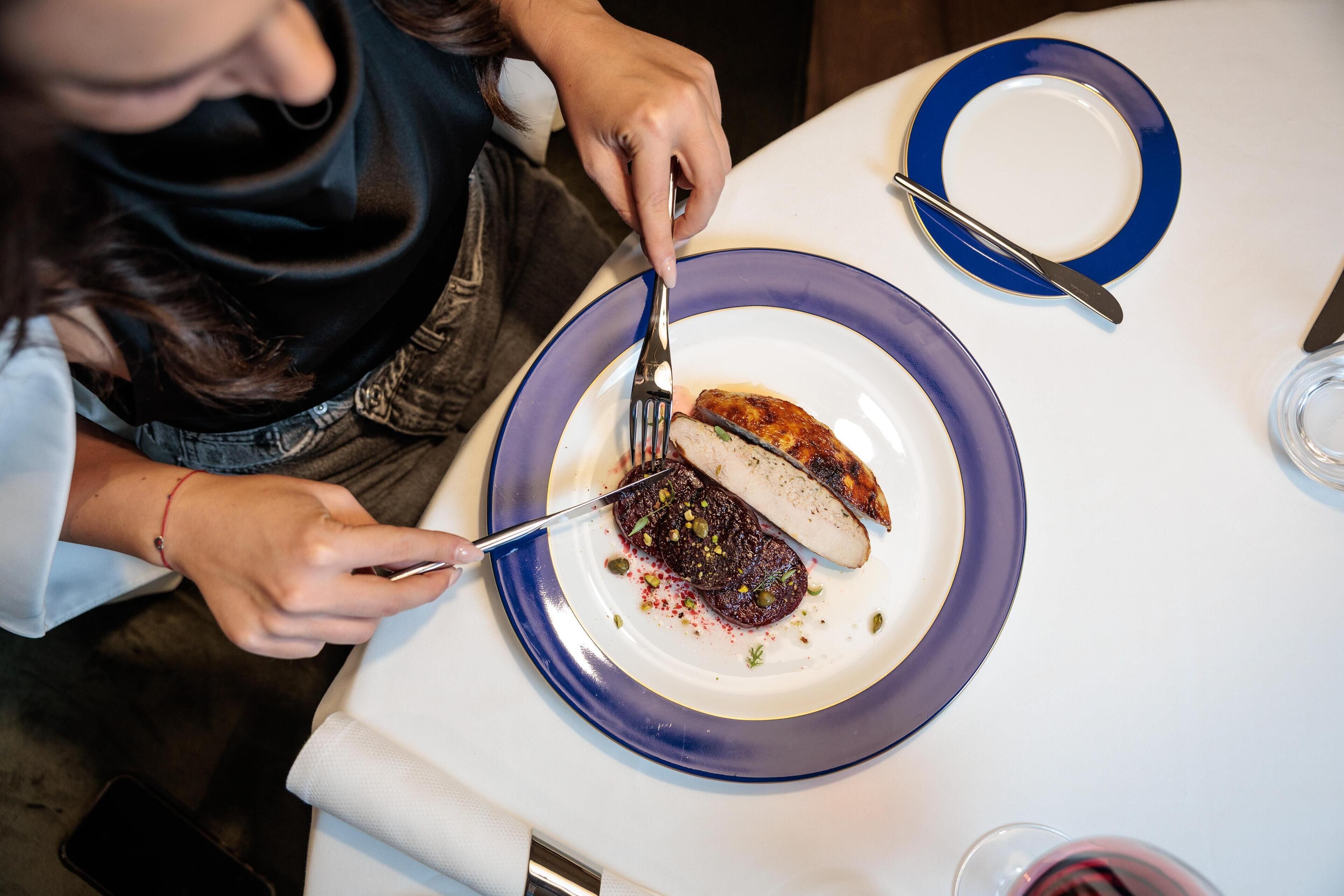 A person cutting a piece of meat on a plate with a fork and knife.