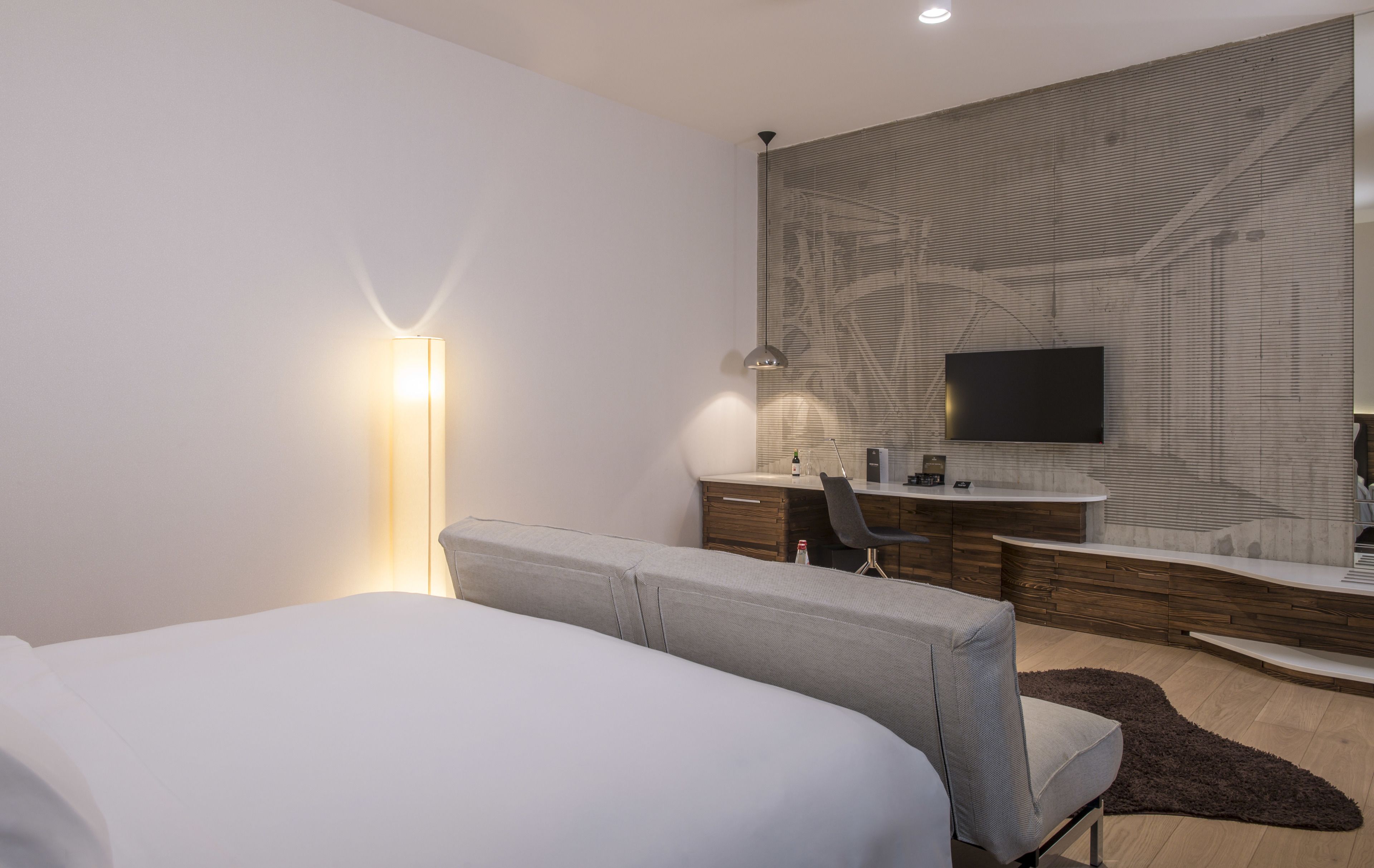 A modern hotel room with a large bed, a desk with a computer, a flat-screen TV, and a wall-mounted mirror.