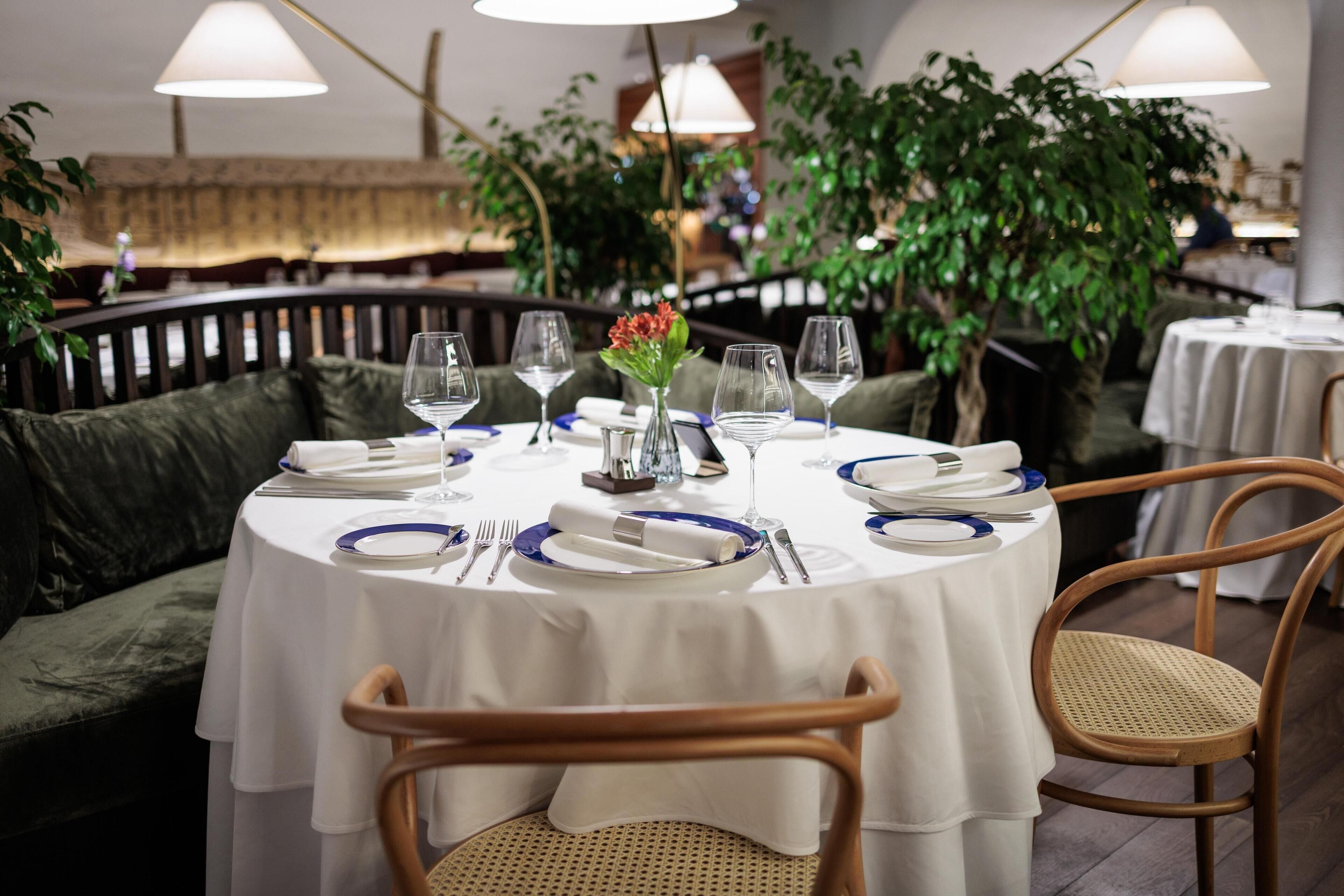 A round dining table with white tablecloth, blue plates, and clear wine glasses set for four.
