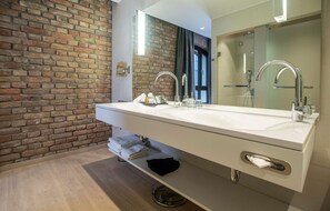 A modern bathroom with a brick wall, a large mirror, a double sink, and a towel rack.