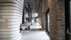 A modern interior with a curved wall displaying a directory, a brick wall, and a long corridor with seating areas. - Radisson Collection Hotel, Old Mill Belgrade (Belgrade)