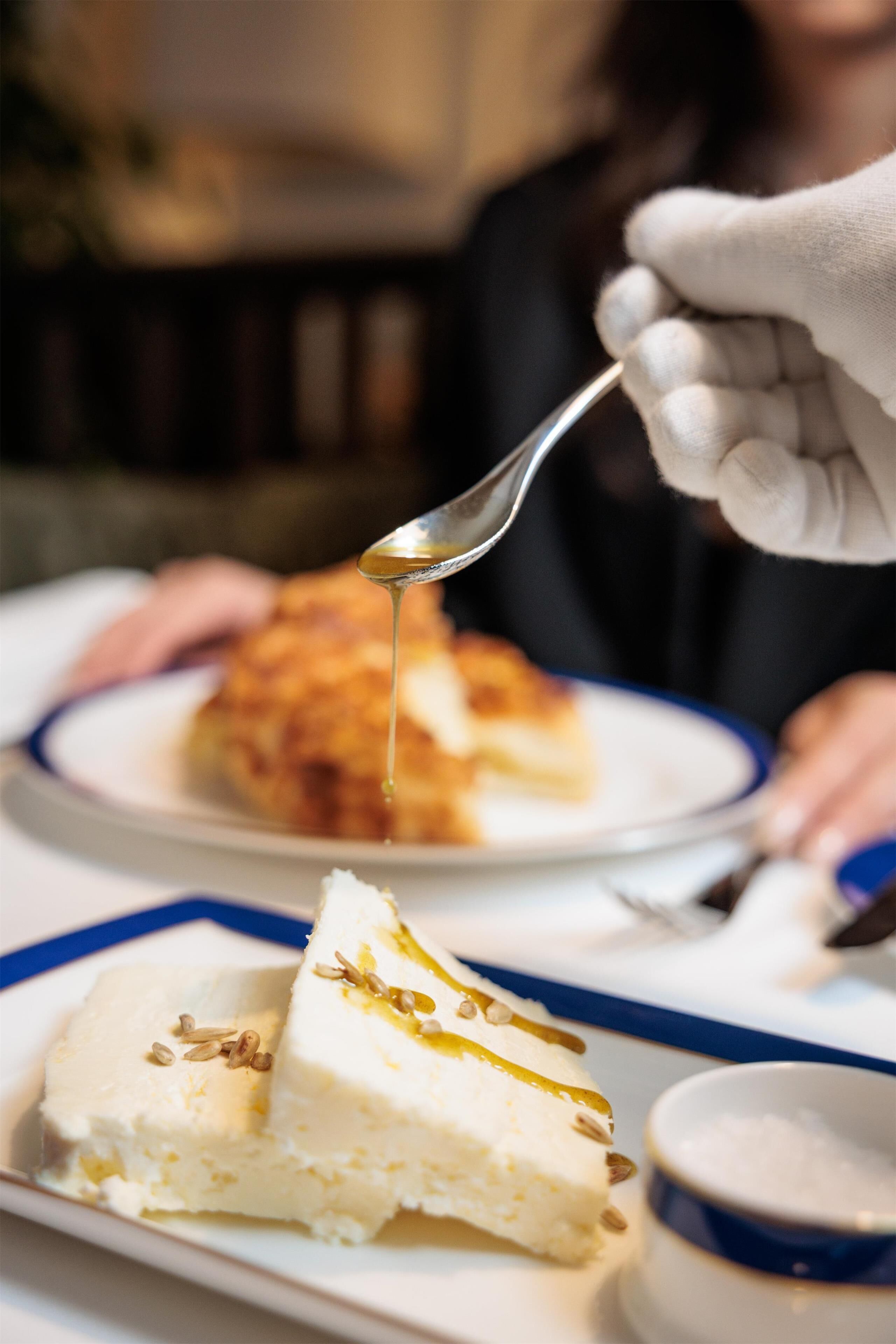 A dessert with a spoonful of syrup being lifted, a bowl of sugar, and a slice of cake on a plate.