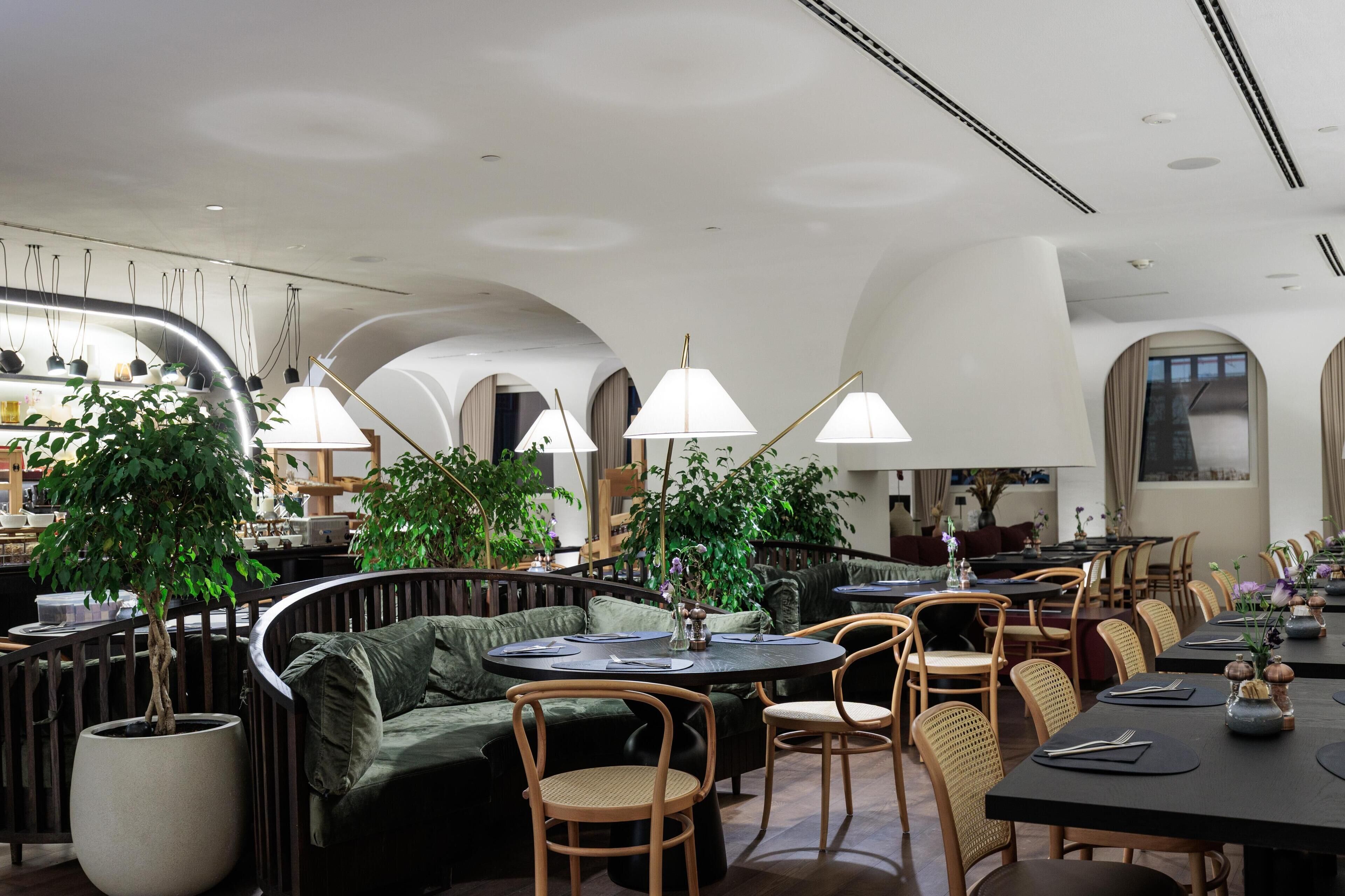 Un ristorante moderno con tavoli rotondi, sedute imbottite e lampade a sospensione.