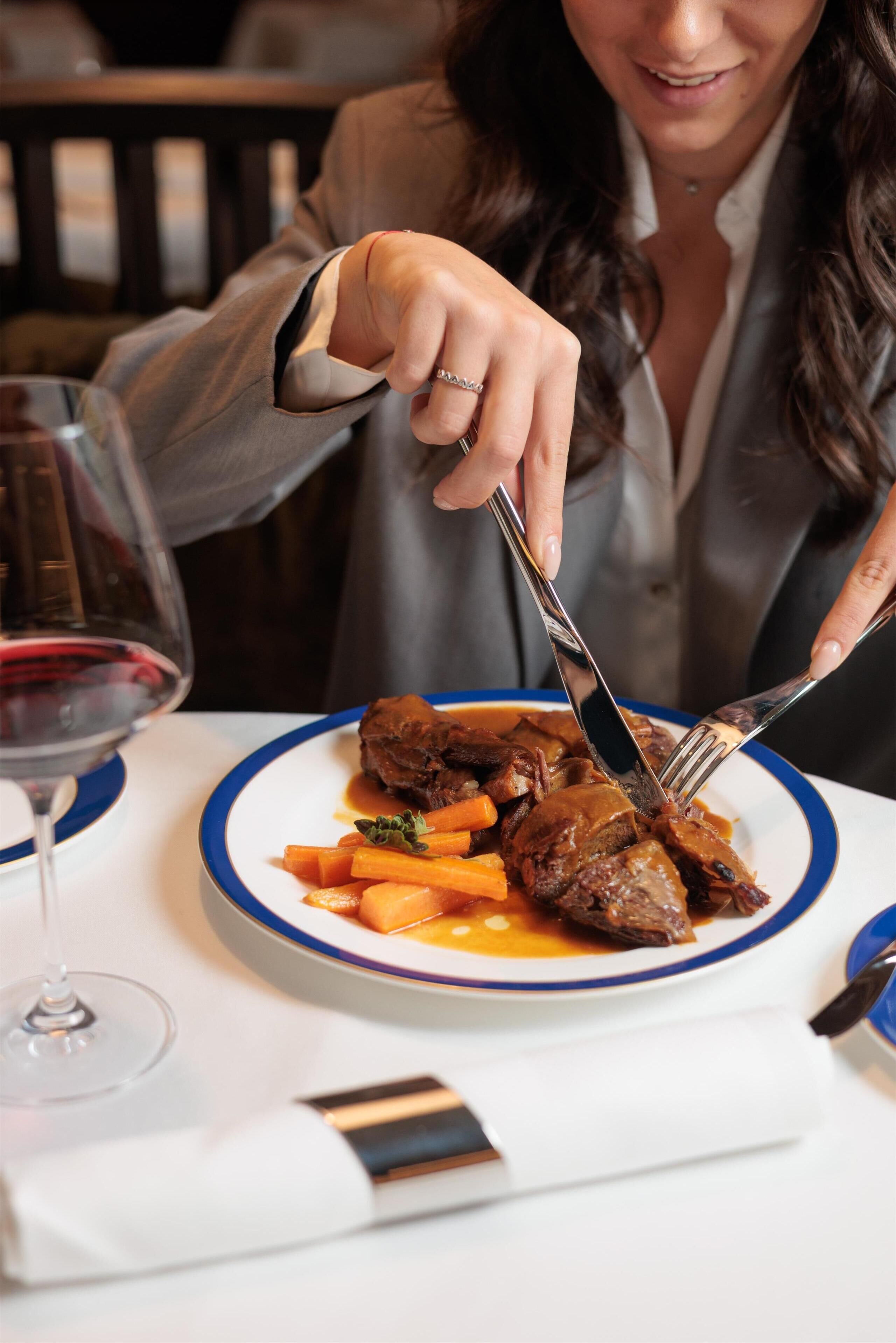 Una persona sta cenando a tavola, con un piatto di cibo, un bicchiere di vino e posate.