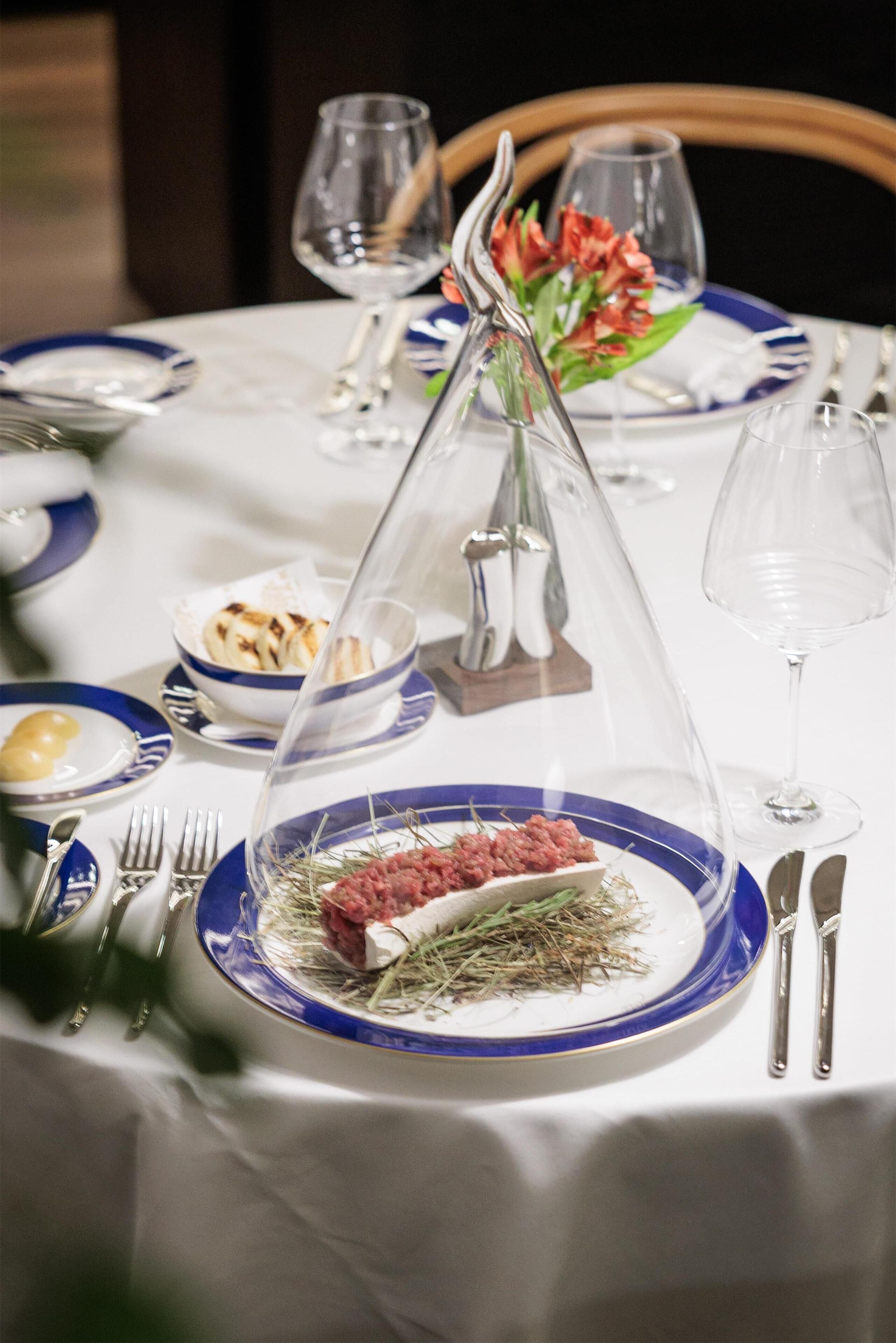 A table set with blue and white plates, silverware, and a clear glass dome over a dish of food.