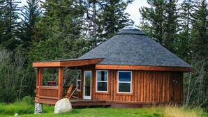A wooden cabin with a conical roof, a porch, and a small deck. - Kenai Peninsula Suites (Homer)