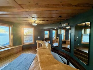 A room with wooden floors, a curved bench, and multiple windows with views of the outdoors. - Seafarer Cliffside (Homer)