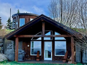 A cabin with a large front porch, a chimney, and a circular water tank on the roof. - Seafarer Cliffside (Homer)