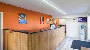 A reception area with a wooden reception desk, a flat-screen TV mounted on the wall, and a water dispenser. - Motel 6 Townsend, GA (Townsend)