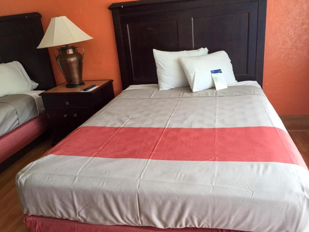 Ein Hotelzimmer mit Bett, Nachttisch, Lampe und Kissen.