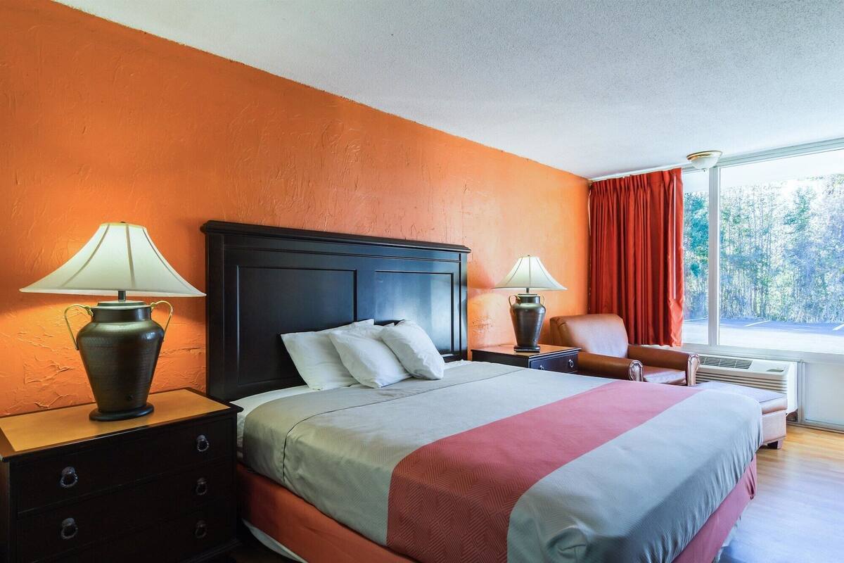 A hotel room with a large bed, two bedside tables with lamps, a chair, and a window with curtains.