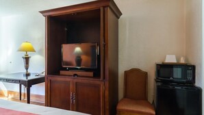A hotel room with a wooden wardrobe, a television, a desk with a lamp, a chair, and a refrigerator. - Motel 6 Townsend, GA (Townsend)