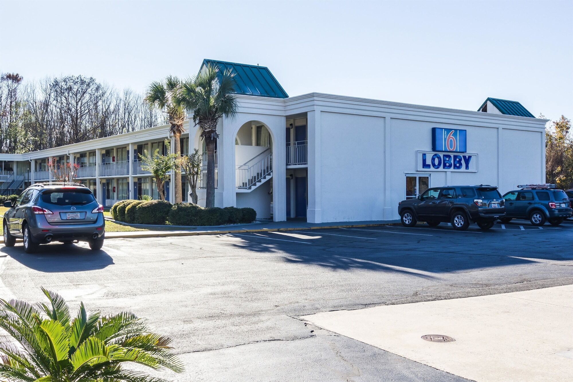 Un motel avec une enseigne indiquant « Réception », un parking et un bâtiment doté d’un toit bleu.