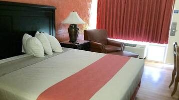 Una habitación de hotel con cama, mesita de noche, lámpara, silla y ventana con cortinas.