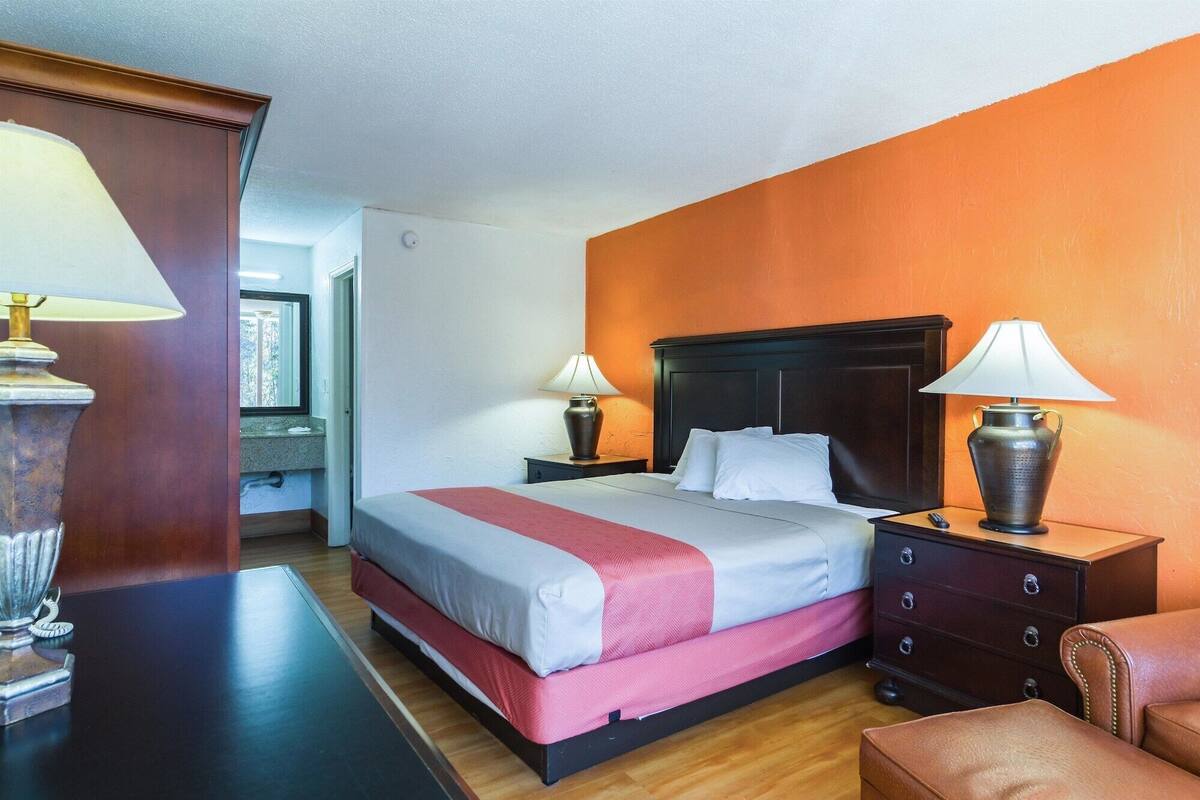 A hotel room with a bed, two bedside tables, a dresser, and a lamp on each table.