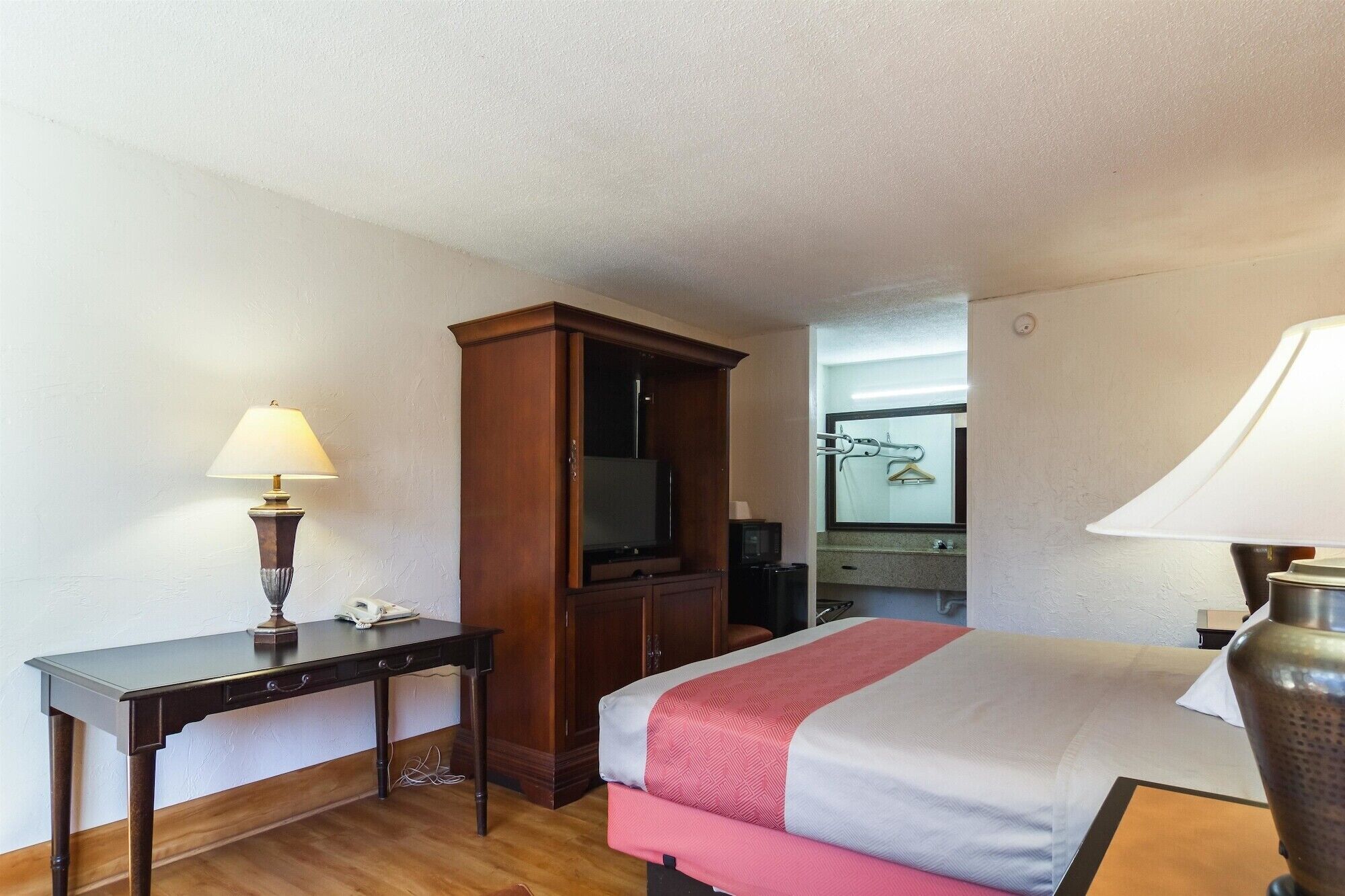 A hotel room with a bed, a desk, a television, and a mirror.