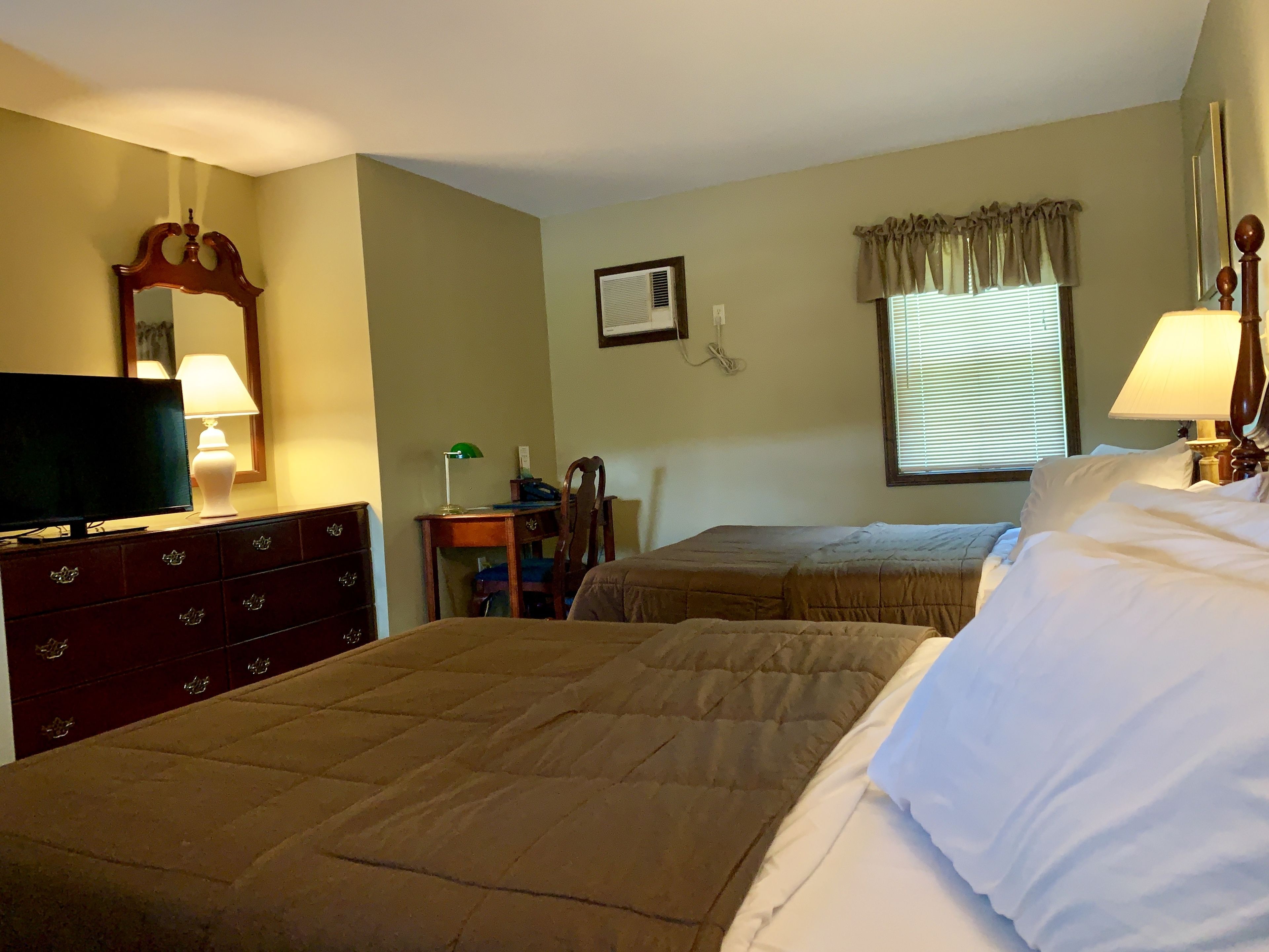 A hotel room with two beds, a dresser, a television, and a desk with a lamp.