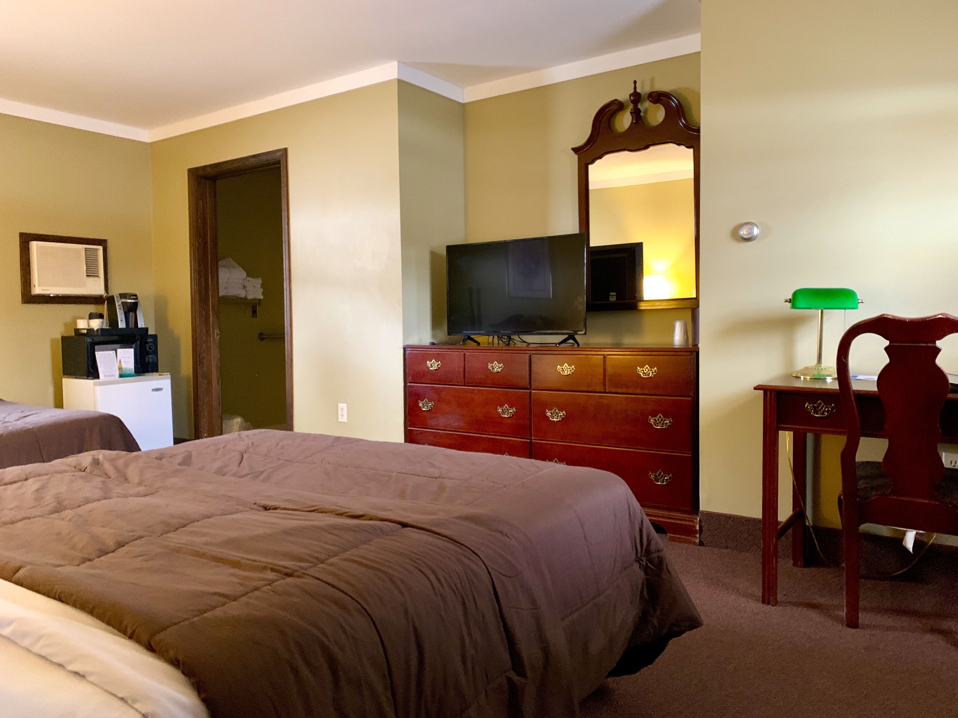 A hotel room with two beds, a dresser with a TV, a desk with a lamp, and a microwave.