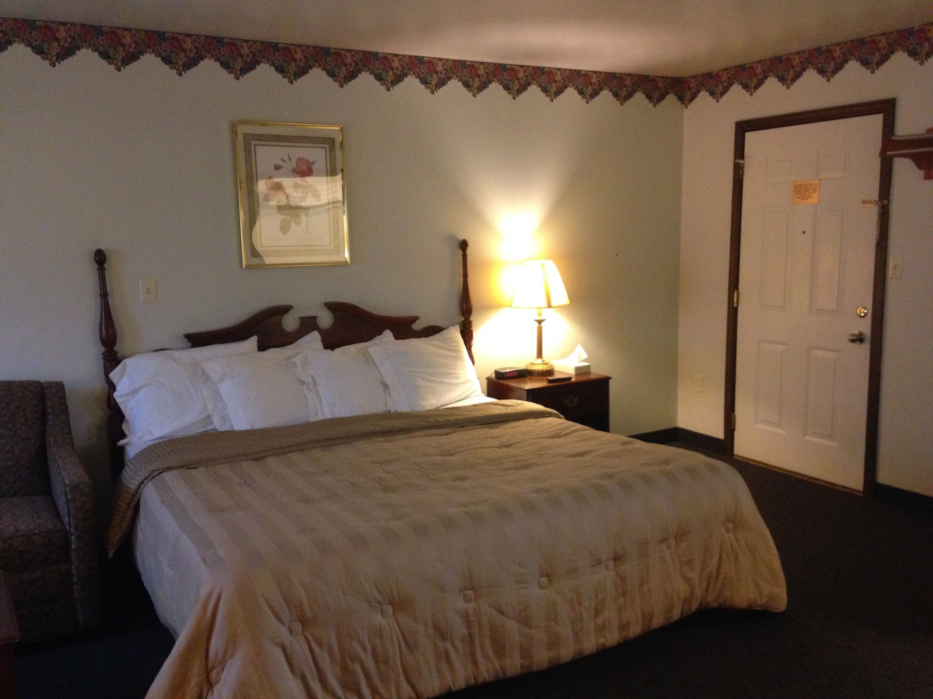 A neatly made bed with a wooden headboard, a bedside lamp, and a framed picture on the wall.