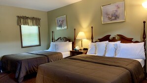Habitación de hotel con dos camas, una mesita de noche con lámpara y dos cuadros enmarcados con motivos florales en las paredes.