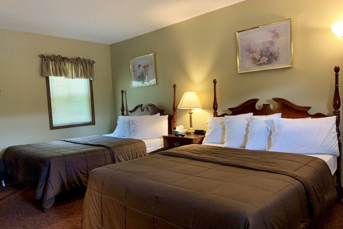 Une chambre d’hôtel avec deux lits, une table de chevet avec une lampe et deux tableaux représentant des motifs floraux, encadrés et accrochés aux murs.